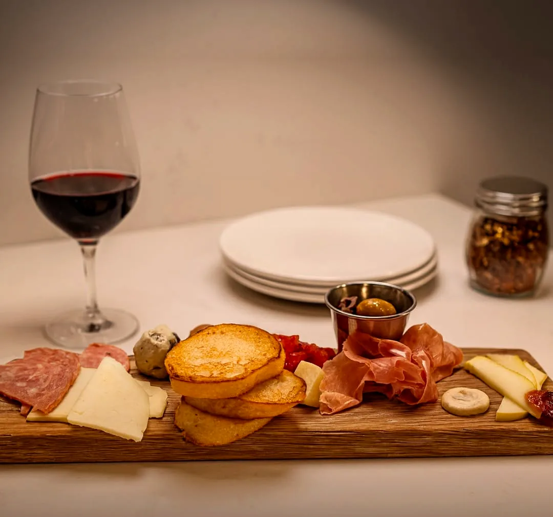 A board of cured meats, cheese and olives beside a glass of red wine