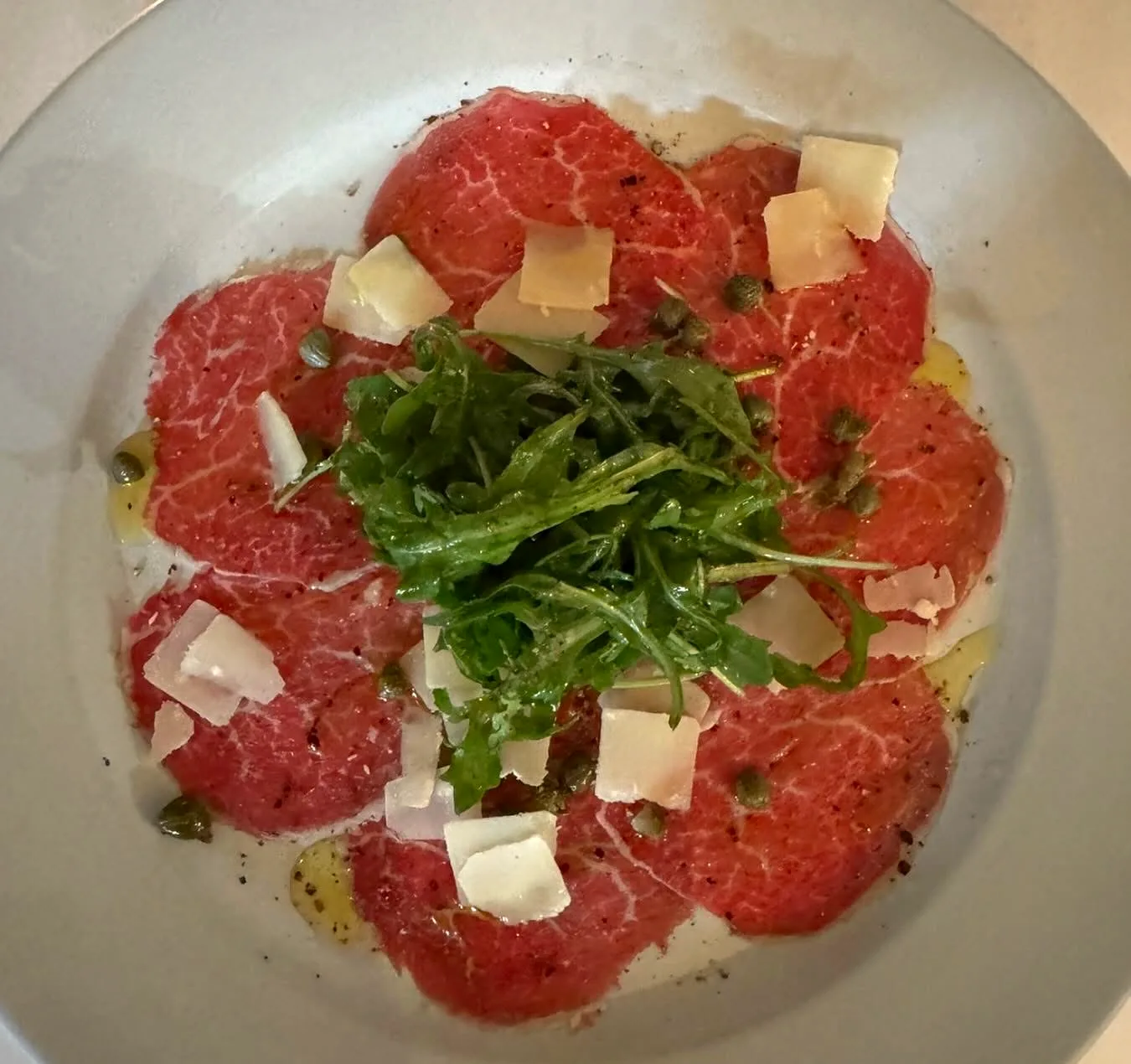 Beef carpaccio fanned around a pile of arugula with shaved cheese and capers