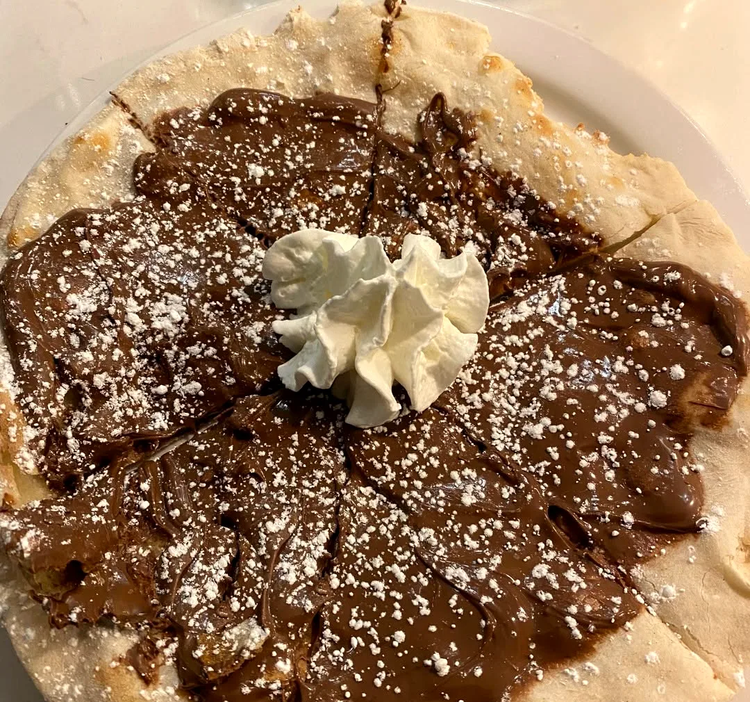 A chocolate dessert galette dusted with sugar under a spoon of cream