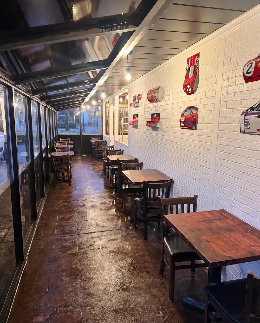 The covered side patio: two-tops down a white brick wall hung with race car panels