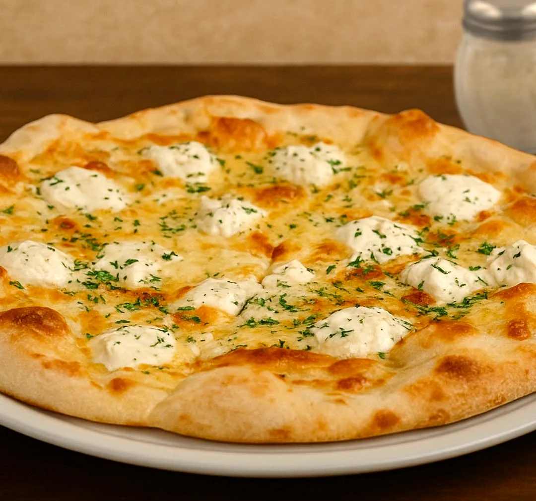 A white pizza dotted with ricotta and herbs on a dark wood table
