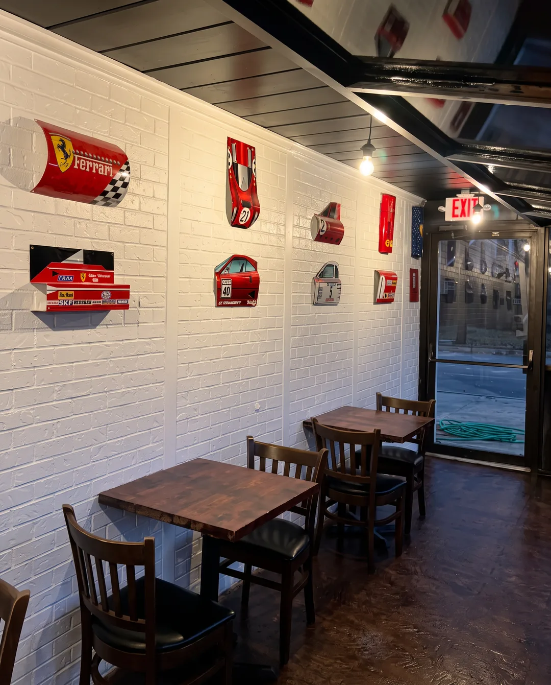 Painted white brick wall hung with cut-out Ferrari race car panels above dark wood tables