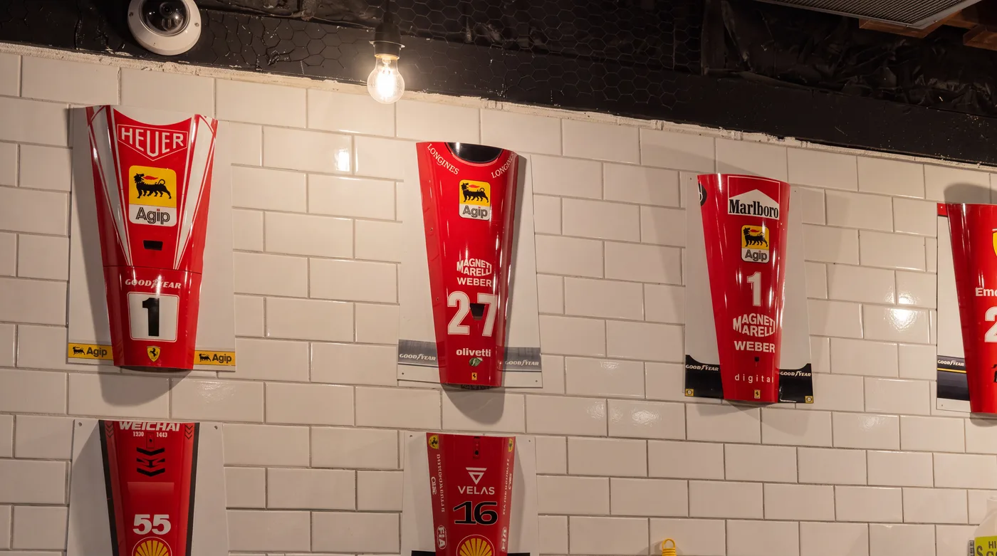 Ferrari Formula One nose cones mounted in two rows along a white subway-tiled wall inside La Scuderia